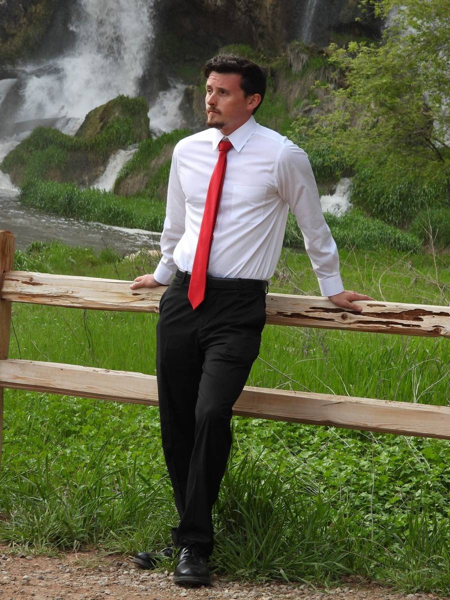 Groom in a red tie leaning on a fence